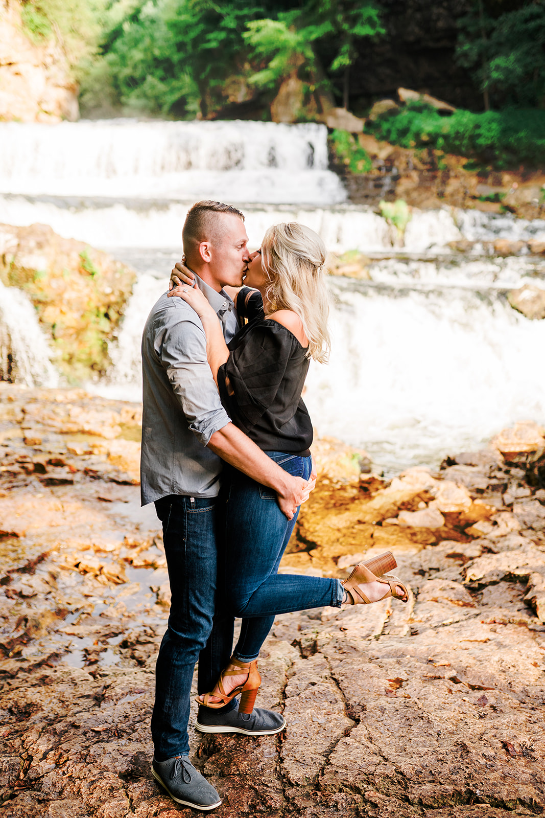 Two couples share intimate kisses against the backdrop of a cascading waterfall. The rushing water creates a serene ambiance as the couples express their affection, surrounded by the beauty of nature.