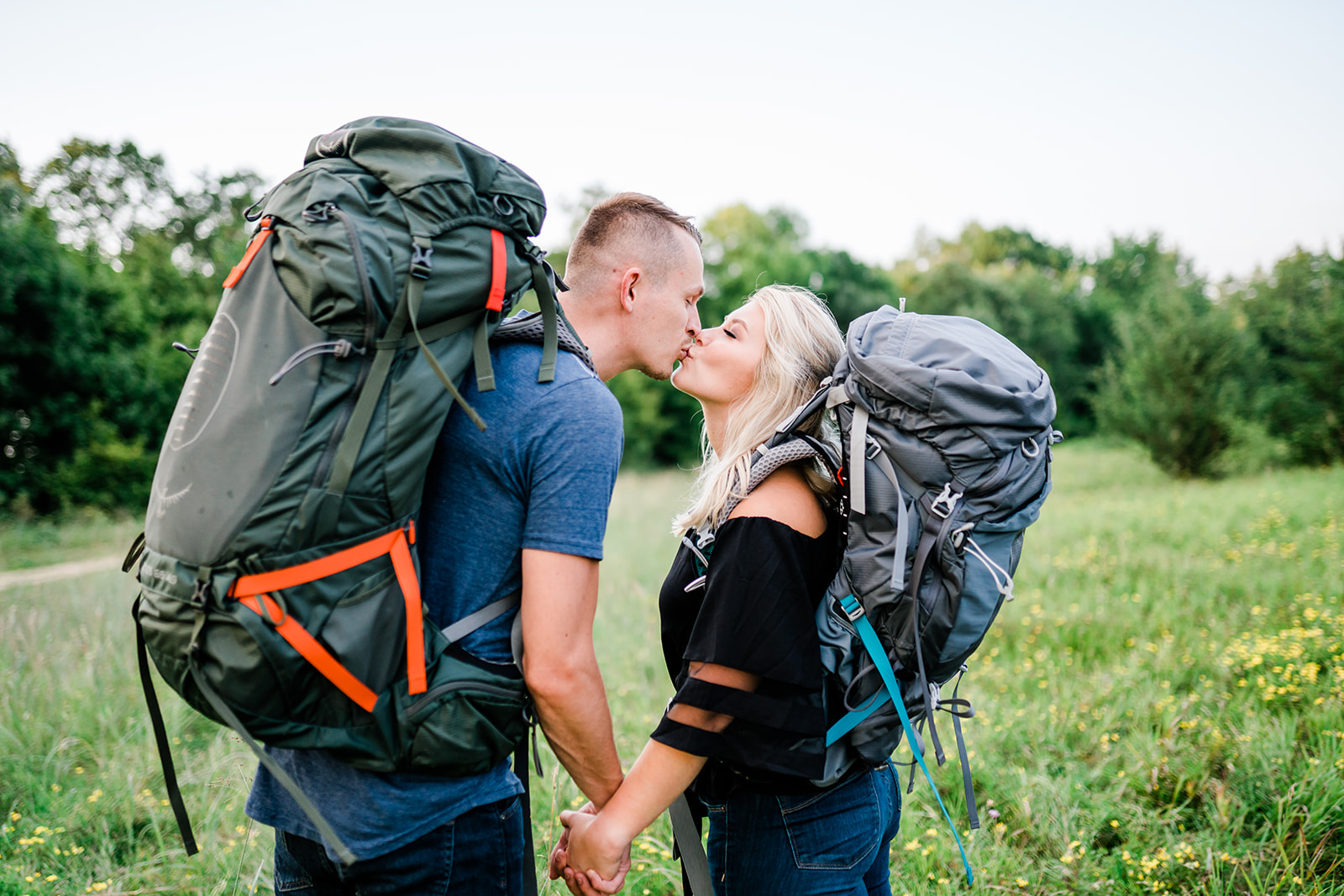 A couple wearing backpacks shares a tender kiss, their love blossoming amidst an adventurous journey. The embrace speaks of companionship and affection, as they pause to celebrate their bond against the backdrop of their outdoor exploration.