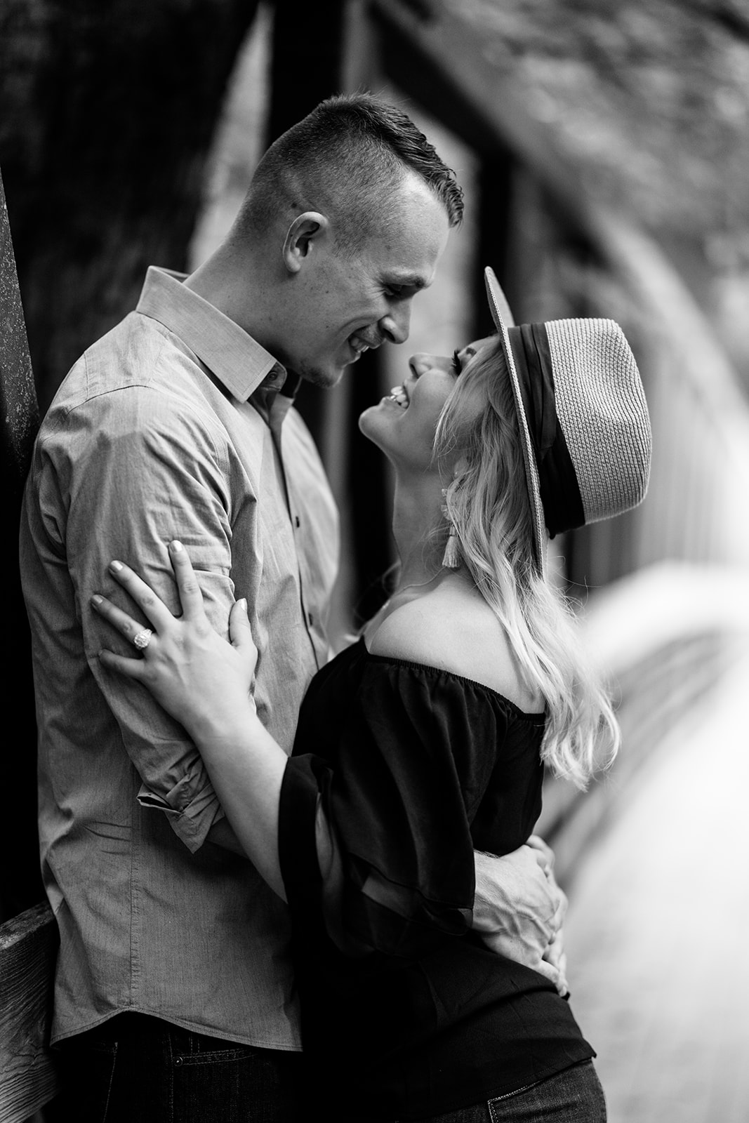Two newly engaged individuals share a moment of joy and affection, gazing into each other's eyes with bright smiles. The woman wears a stylish hat, adding a touch of charm to the scene as they bask in the happiness of their commitment to each other.