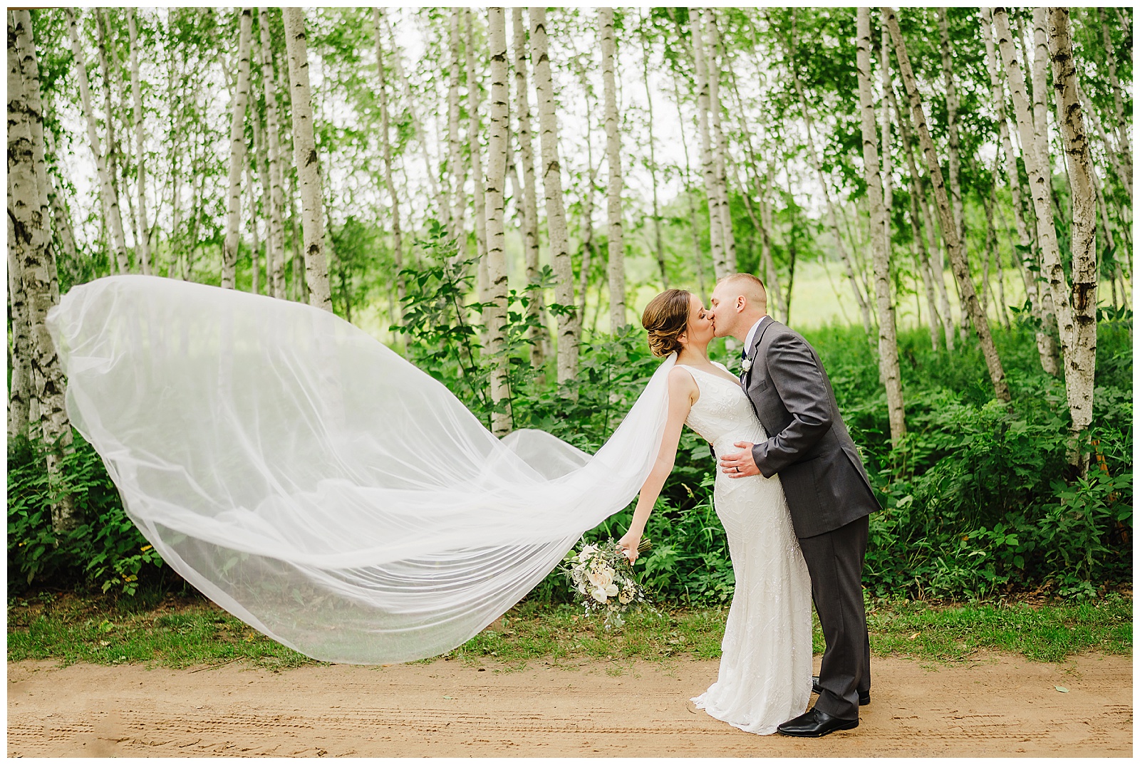 Bride and groom share a kiss while her veil blows in the summer breeze on their wedding day. Chippewa Valley wedding Fall wedding Fall colors #dixonappleorchard #orchardweddingvenue #outdoorwedding #appleorchardwedding #wisconsinweddingvenue