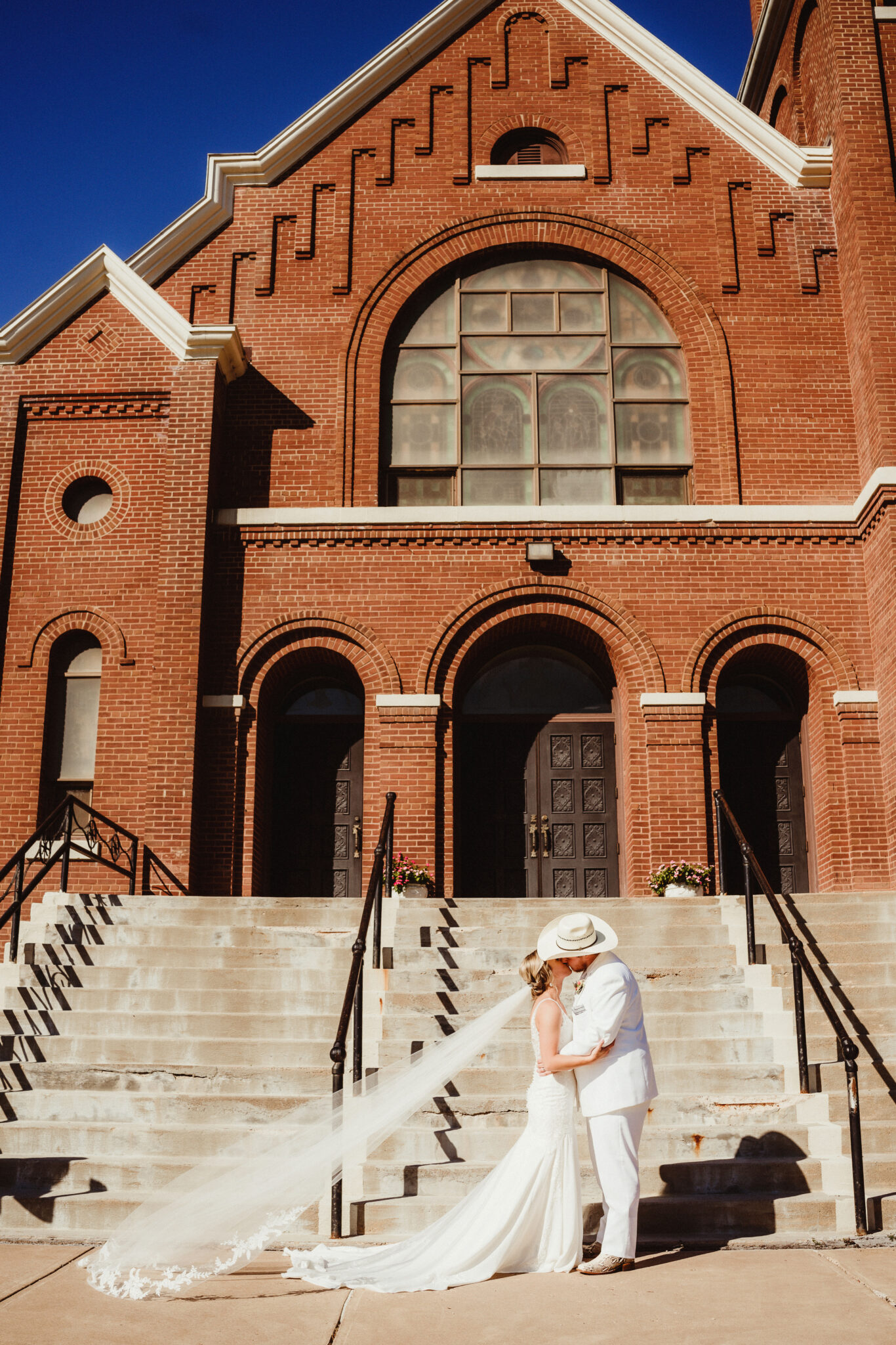 A rustic bride and groom share a kiss in front of their red brick Wisconsin wedding venue. Cowboy wedding Bridal veil photo Church wedding venue Wisconsin #weddingplanning #weddingtimeline #diywedding #wisconsinweddingphotographer #wisconsinchurchwedding