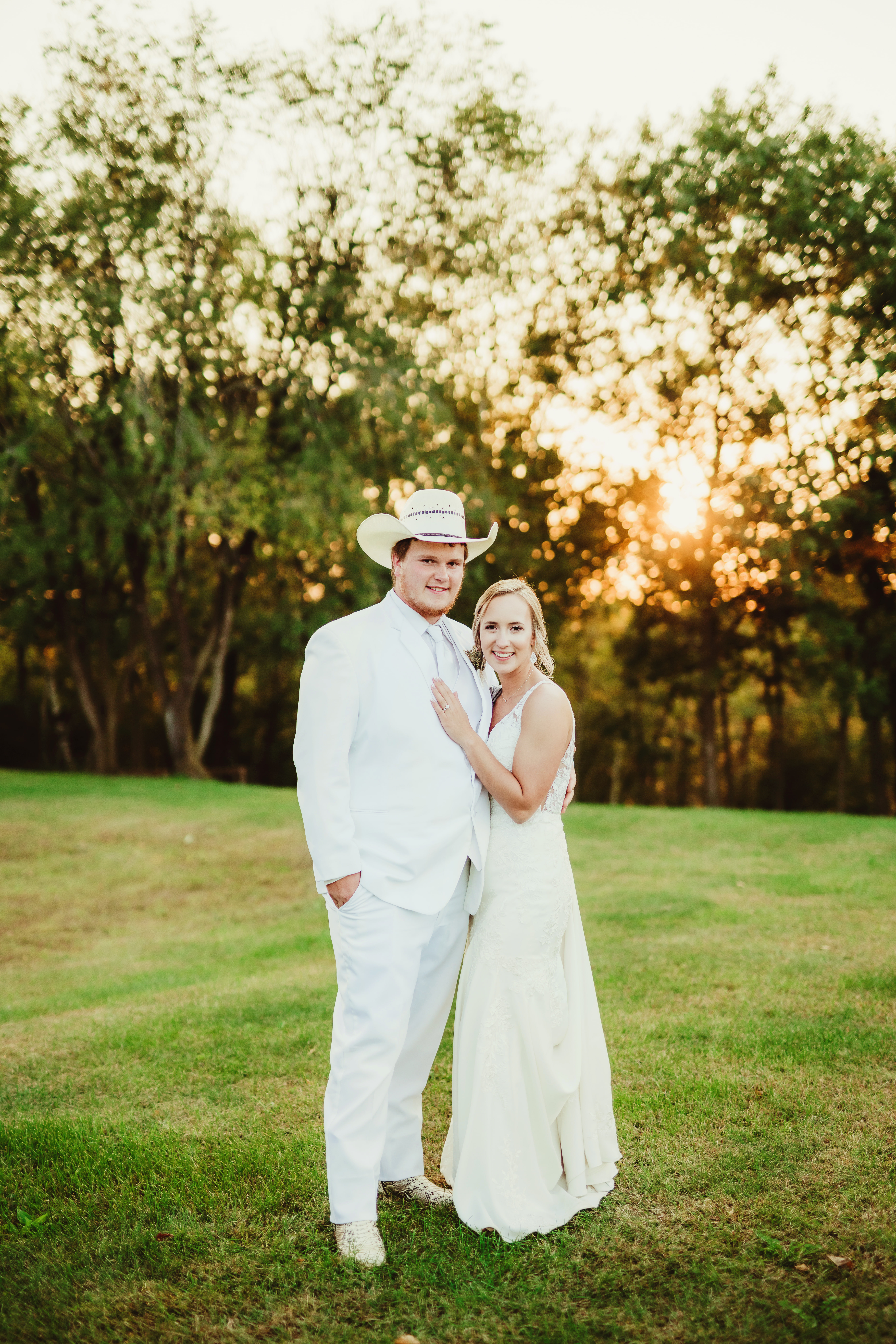 A Wisconsin groom poses with his bride in a white western suit, white cowboy boots, and white cowboy hat. Golden hour bridals Western bride and groom #weddingplanning #weddingtimeline #diywedding #wisconsinweddingphotographer #wisconsinchurchwedding