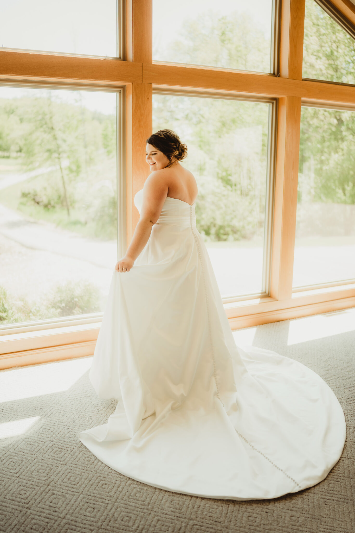 This stunning plus sized bride shows off her wedding dress in front of large venue windows. Natural light Wisconsin bride Sleeveless wedding gown #dixonappleorchard #orchardweddingvenue #outdoorwedding #appleorchardwedding #wisconsinweddingvenue
