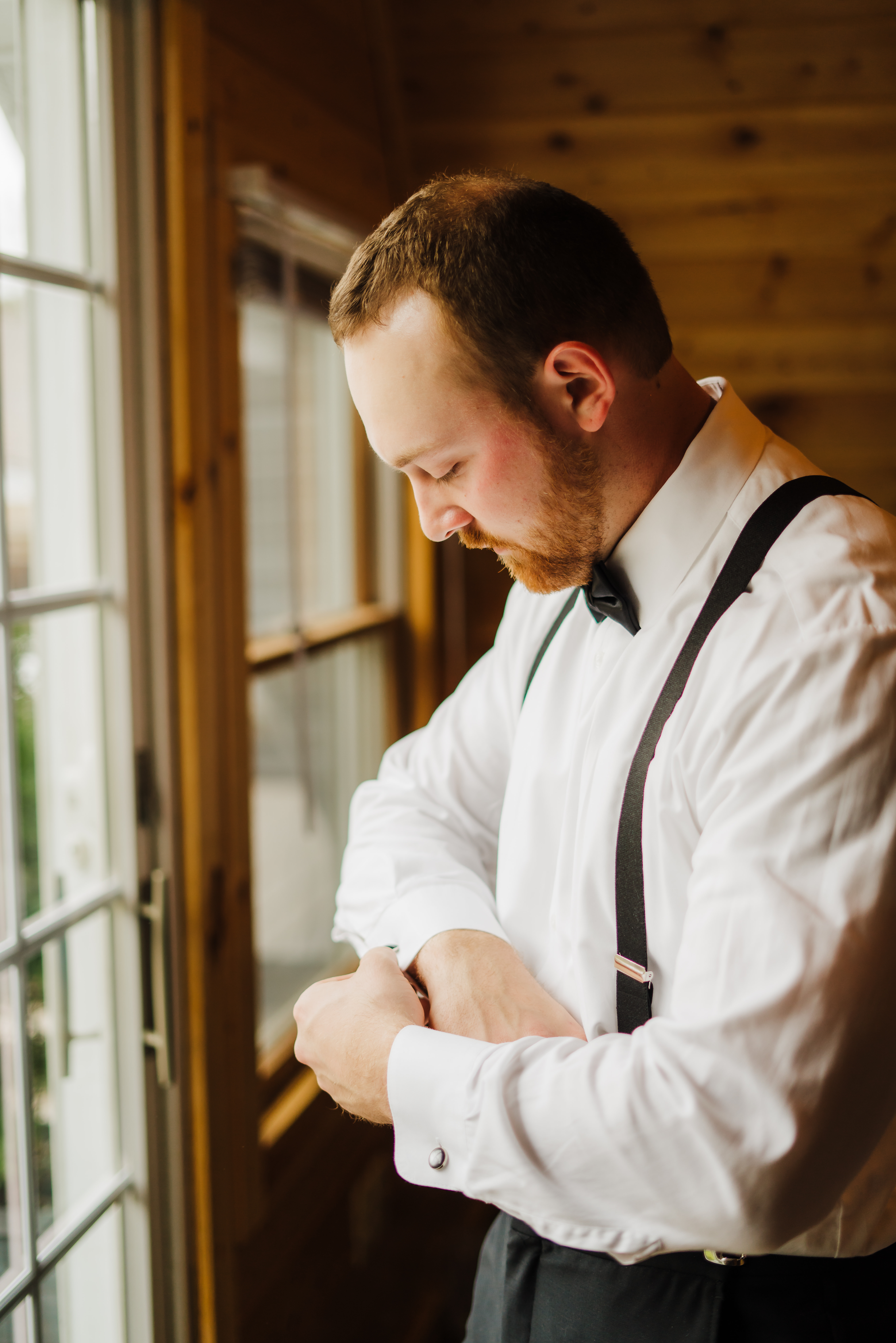 An excited groom gets ready for his forest green wedding ceremony in black suspenders and a bowtie. Groom outfit inspo Rustic wood wedding venue #forestgreenwedding #rusticweddingvenue #weddingplanning #wisconsinweddingphotographer #wisconsinweddingvenue