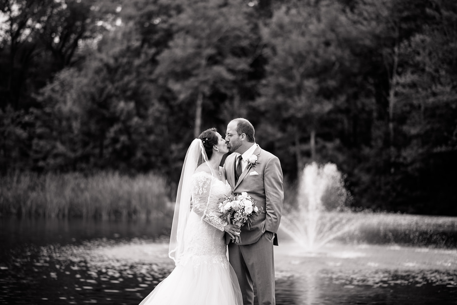 A black and white wedding photo of a bride and groom in front of a pond and fountain.  Black and white wedding photos Outdoor bridals Bride and groom pose #dixonappleorchard #orchardweddingvenue #outdoorwedding #appleorchardwedding #wisconsinweddingvenue