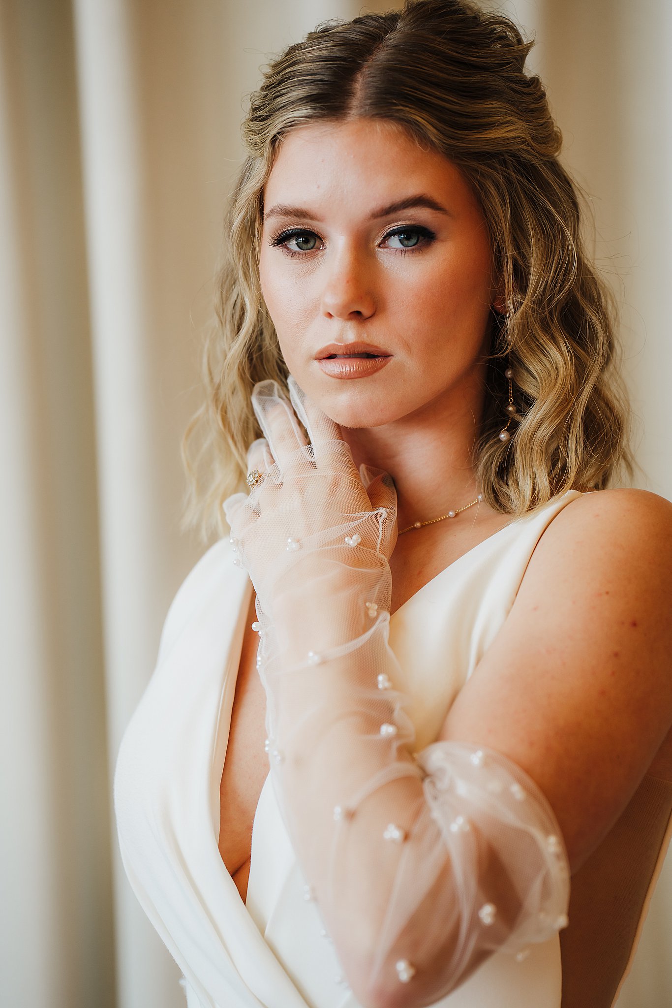 A stunning bride wearing a glove gently touches her cheek as she gazes into the camera, radiating elegance and beauty.