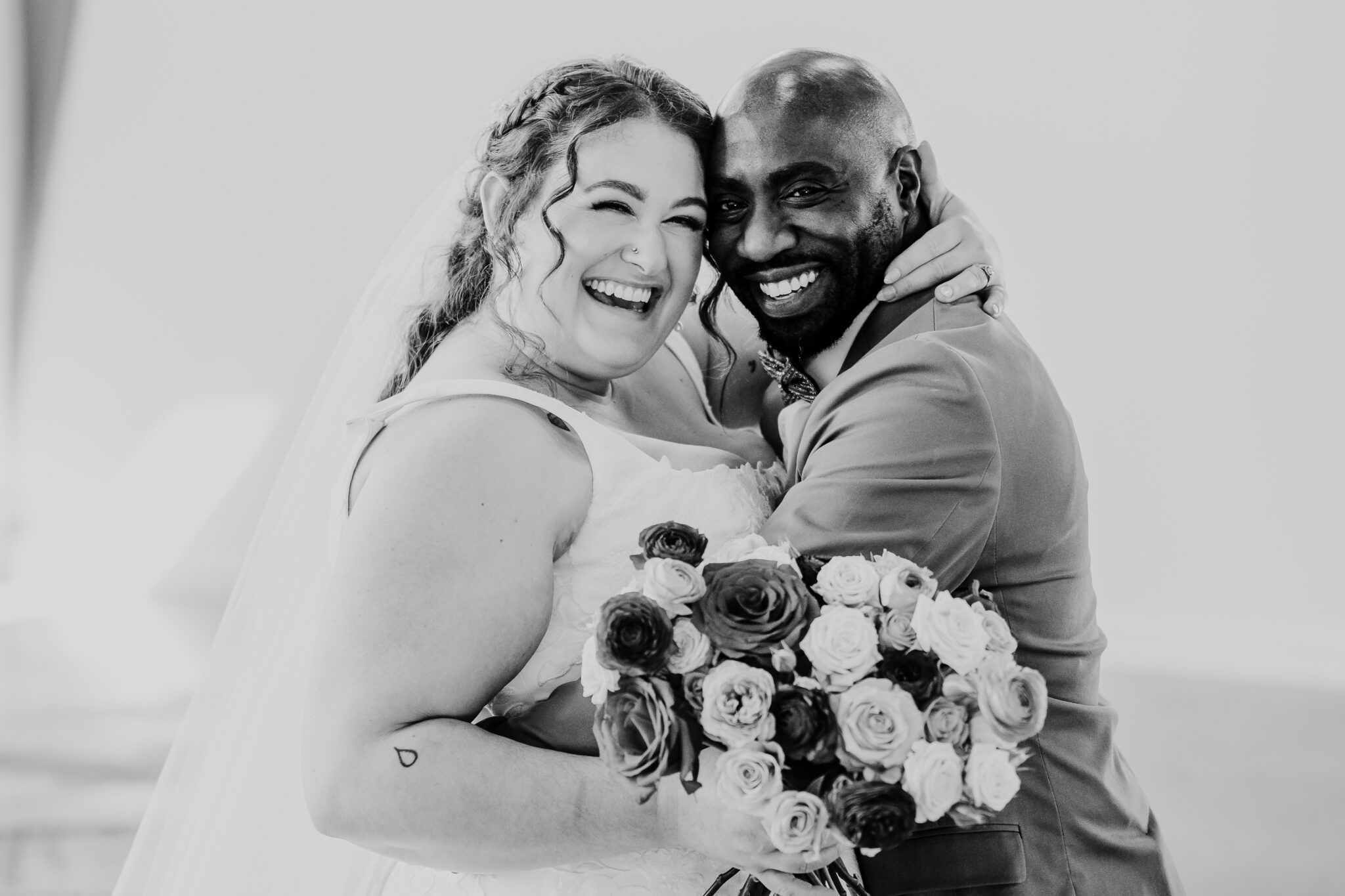 A mixed race couple smile at the camera as they embrace eachother lovingly.