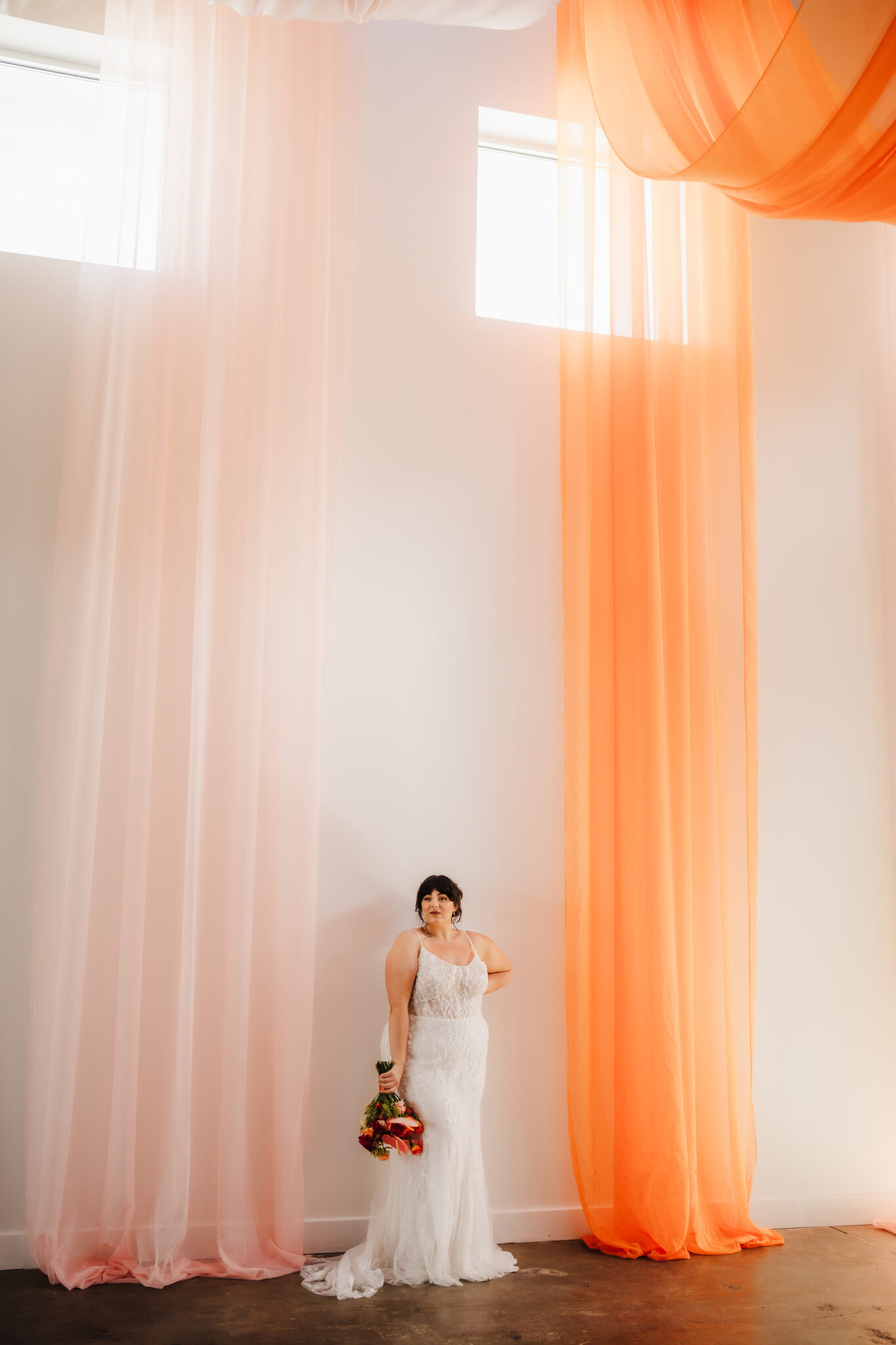 A bride poses around drapery as she stairs off into the room. 