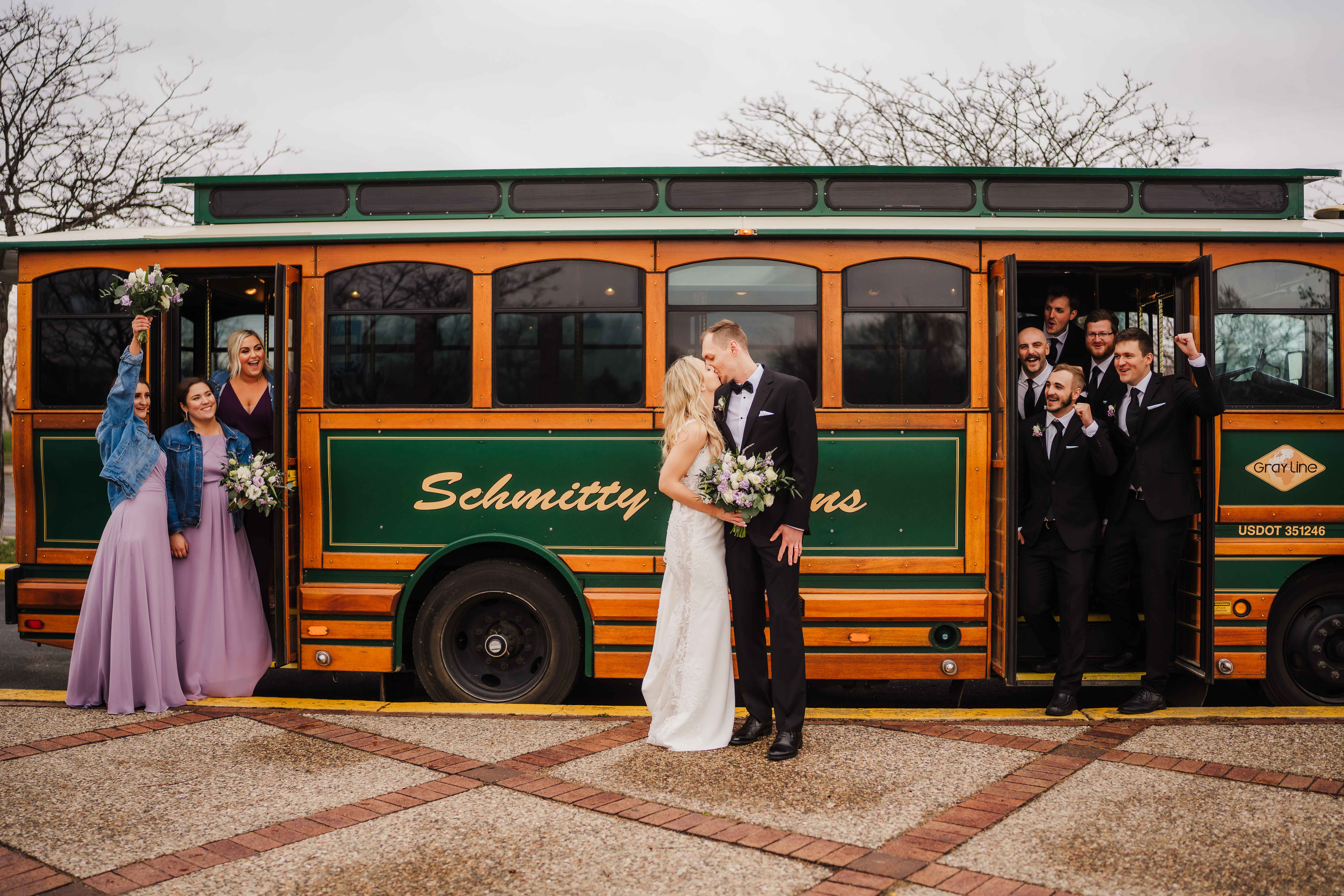 A couple, accompanied by their bridal party, stands in front of a trolley in Minneapolis, ready to embark on a journey of love and celebration. The group radiates happiness and excitement as they pose for a memorable photo in the vibrant cityscape.
