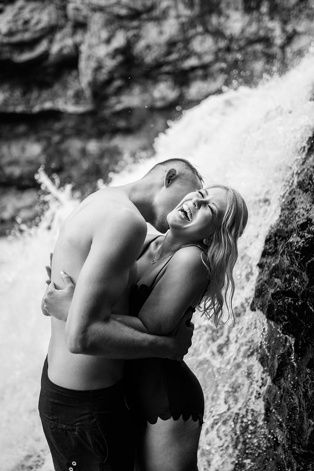 A romantic moment between an engaged couple as the man kisses the woman's neck affectionately under a cascading waterfall.