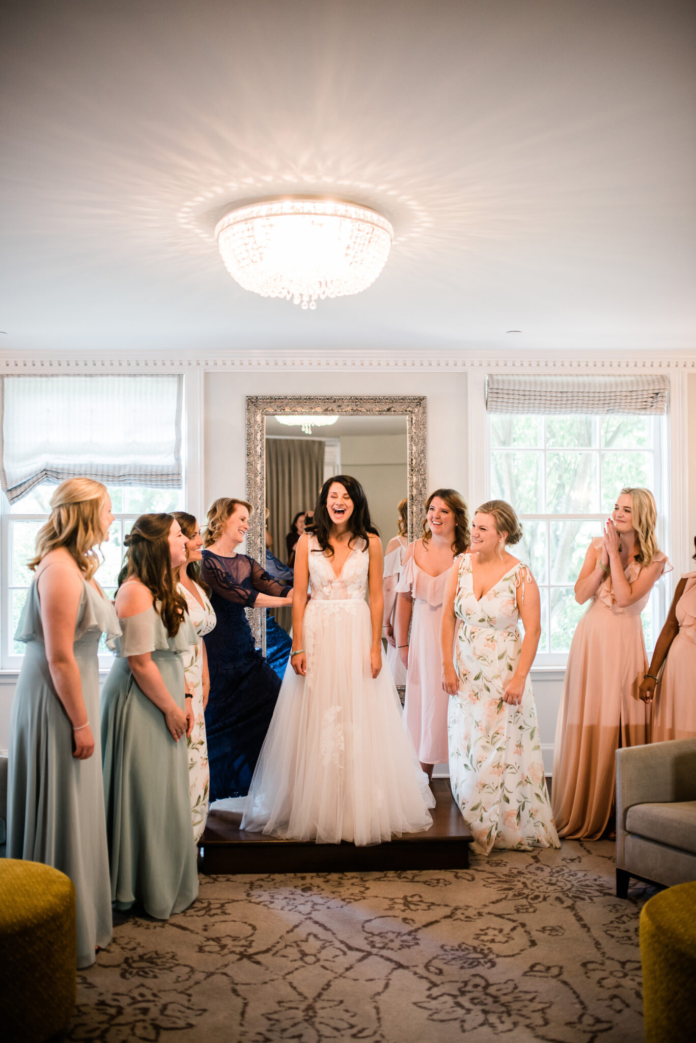 A bride is surrounded by her bridesmaids laughing with intense joy as she gets into her wedding gown.