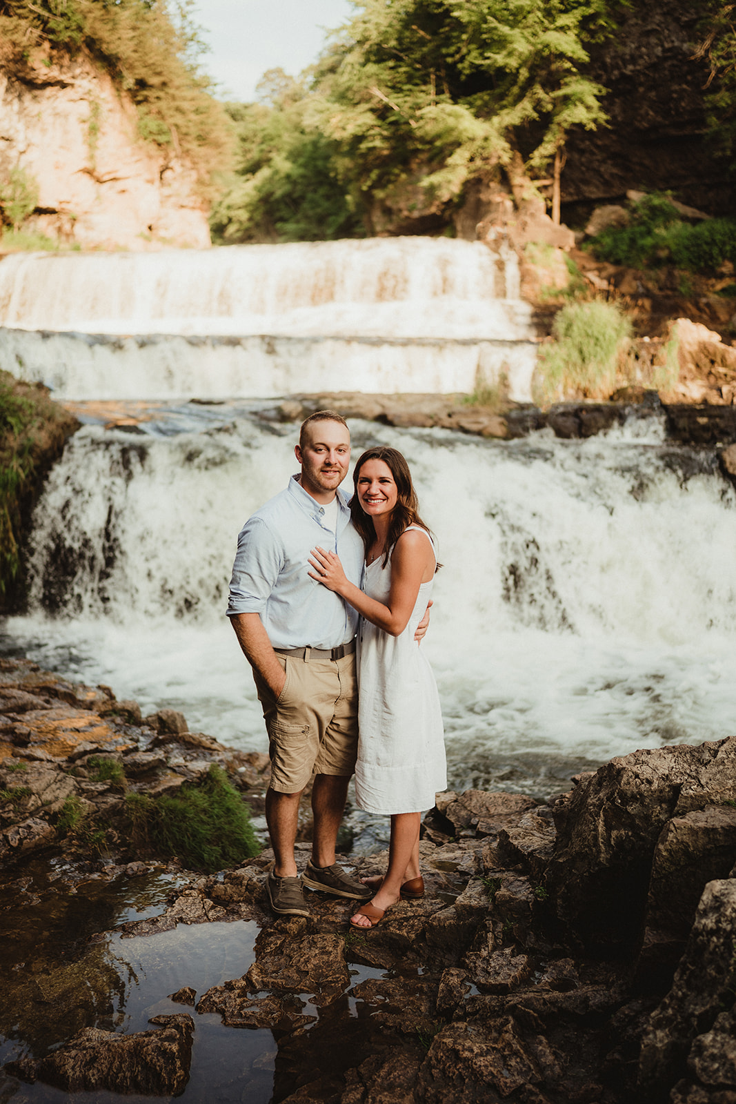 An intimate engaged couple embraces with a stunning waterfall as their backdrop.