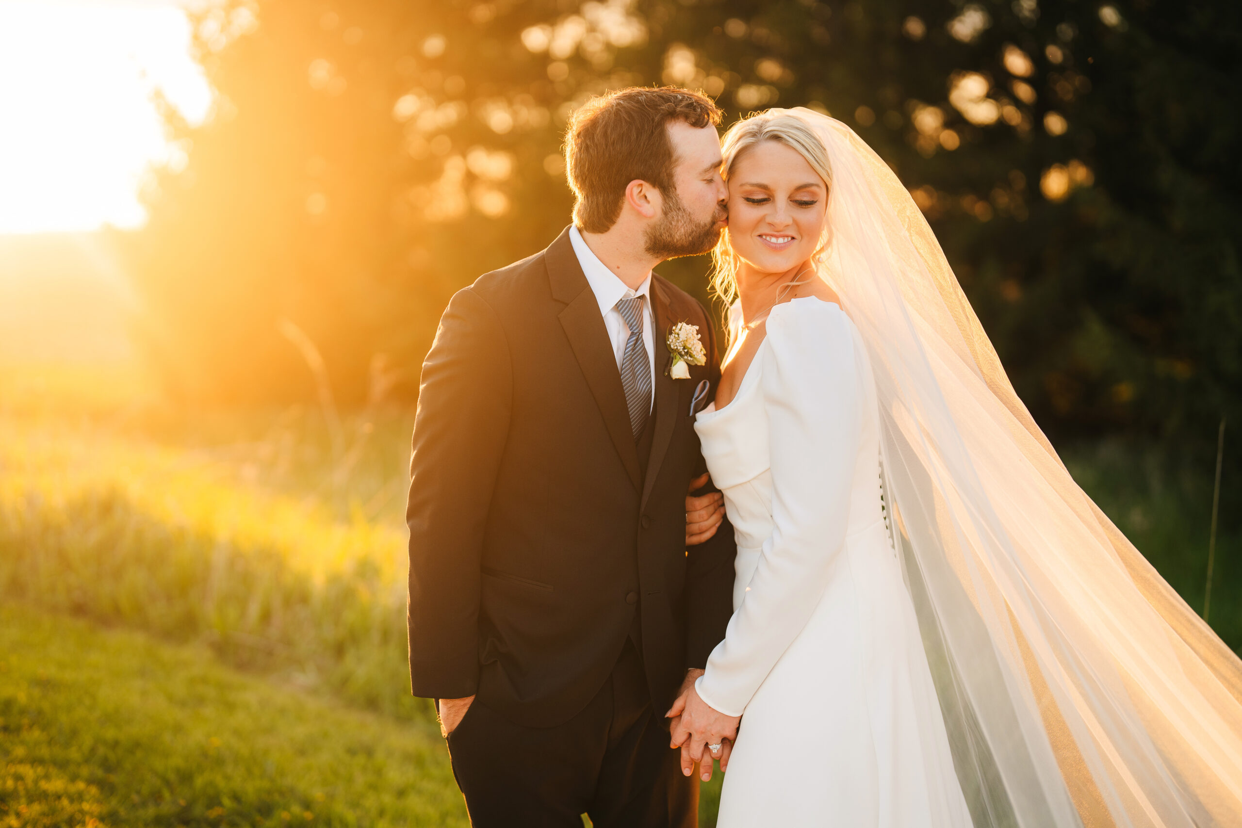 A groom kisses his bride tenderly as the golden sun bathes them in a warm, radiant glow.