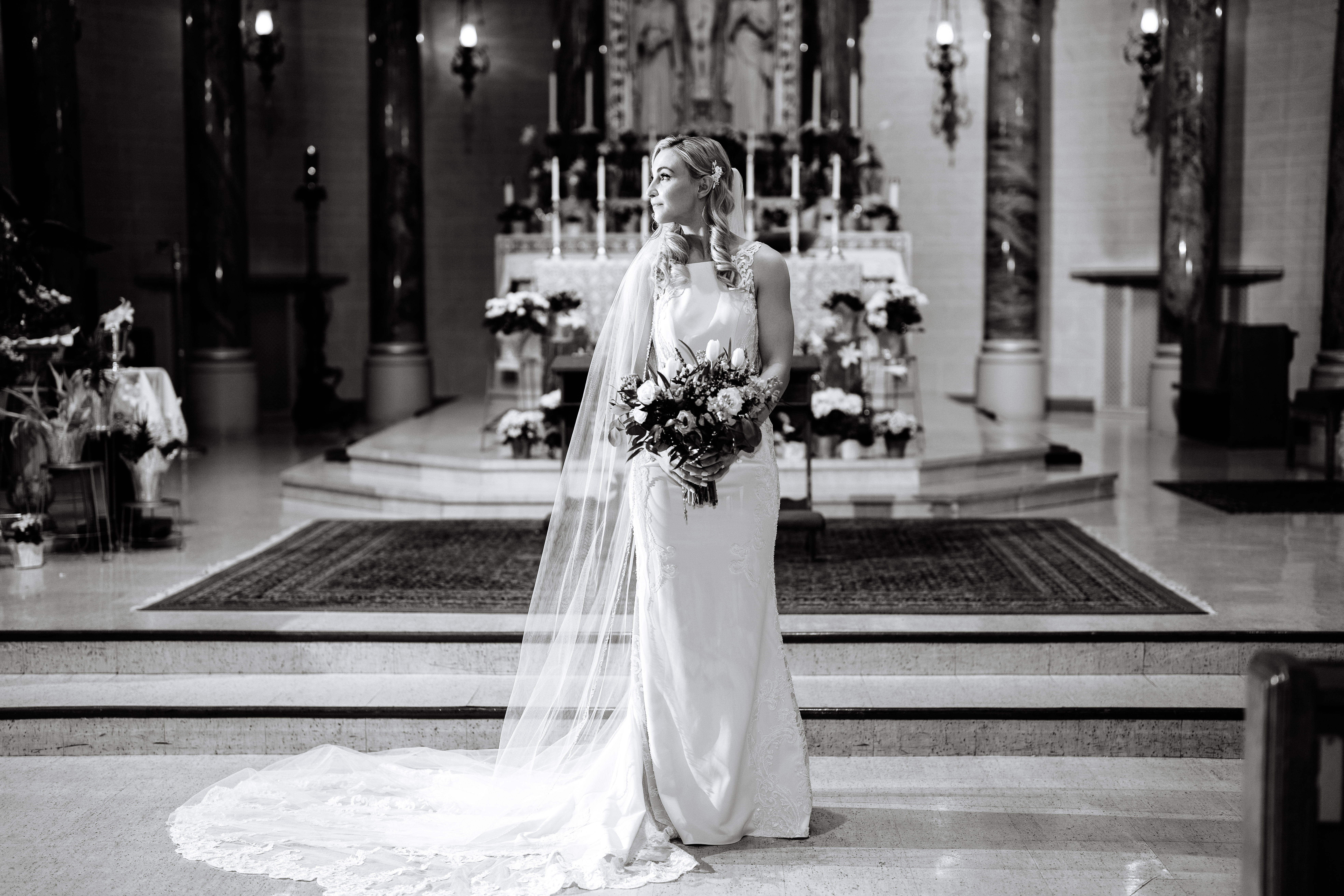 Black-and-white photo of a bride standing in front of the grand altar at St. Paul Cathedral, holding a bouquet with her veil cascading behind her, capturing a timeless and romantic moment in a sacred space.