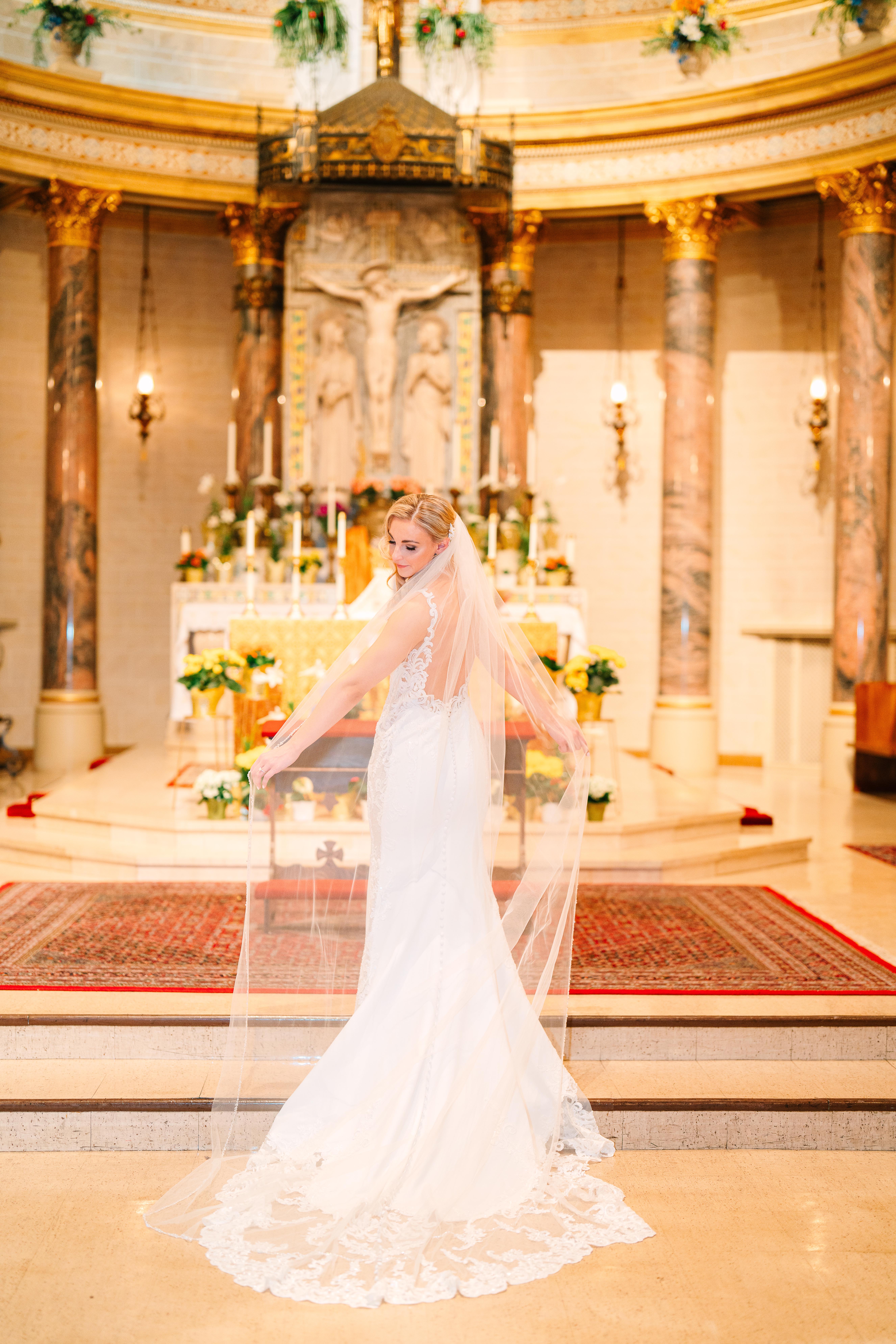 Bride standing gracefully in front of the ornate altar at St. Paul Cathedral, her long veil and elegant gown bathed in soft light, symbolizing timeless romance and the sacred commitment of marriage.