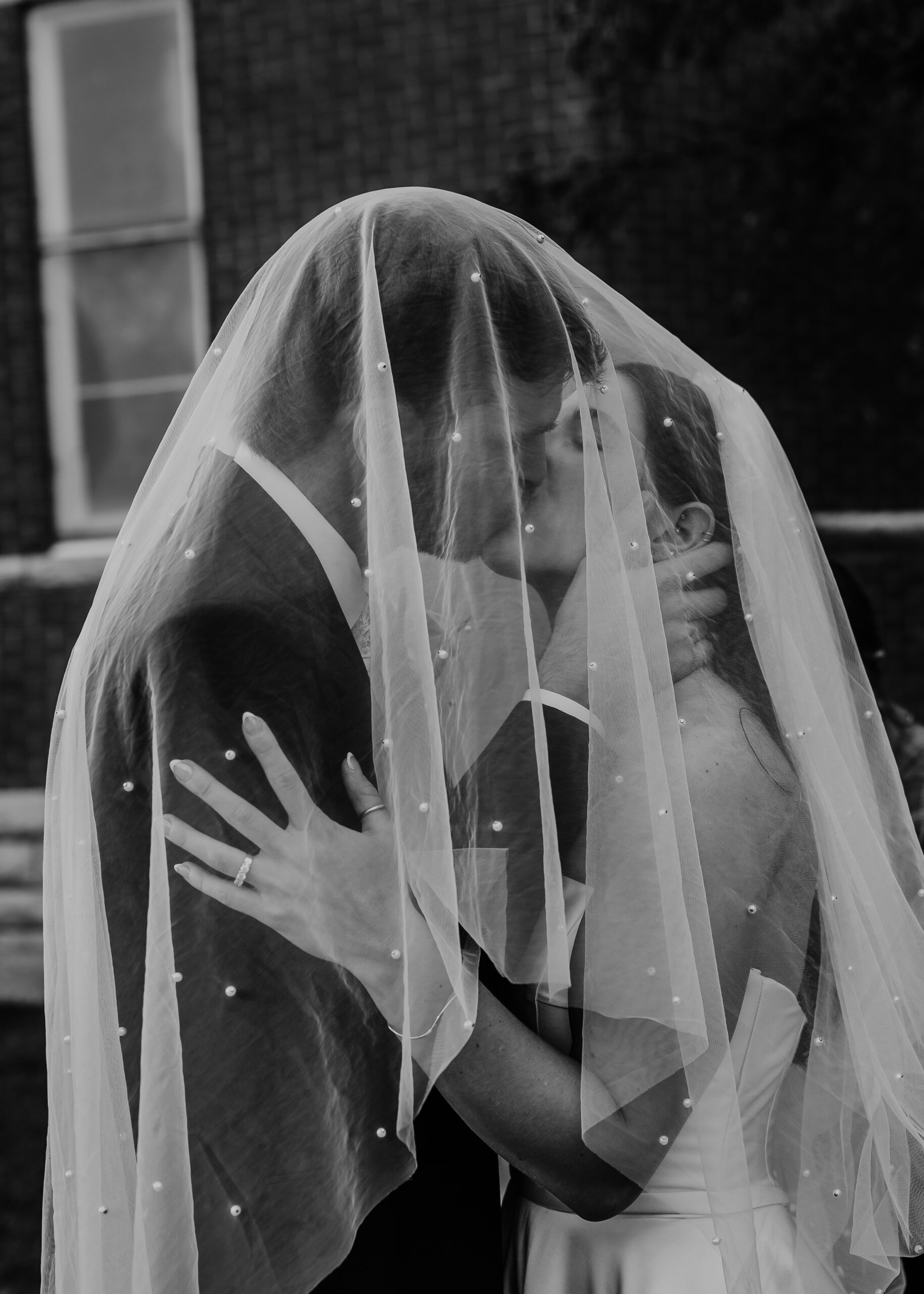 Romantic black and white portrait of a bride and groom under a veil at Cappella Wedding venue in La Crosse Wisconsin captured on city streets after their ceremony
