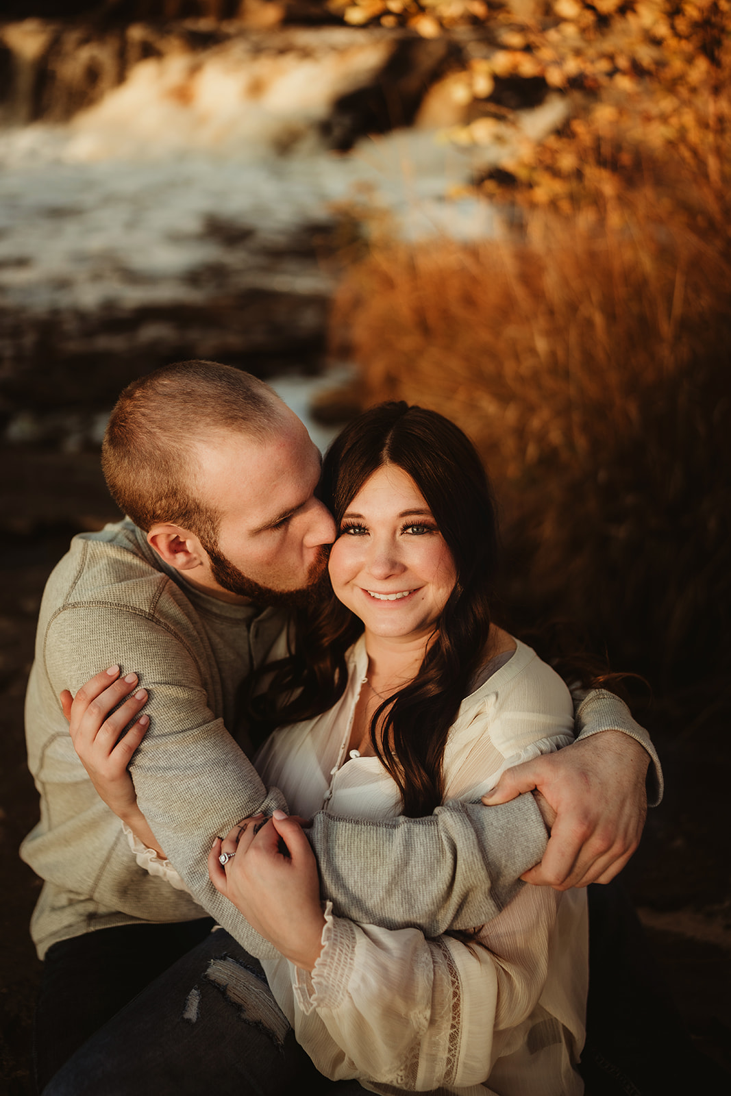 A couple kiss on the side of a waterfall at Big Falls County Park in Eau Claire Wisconsin for an engagement session.