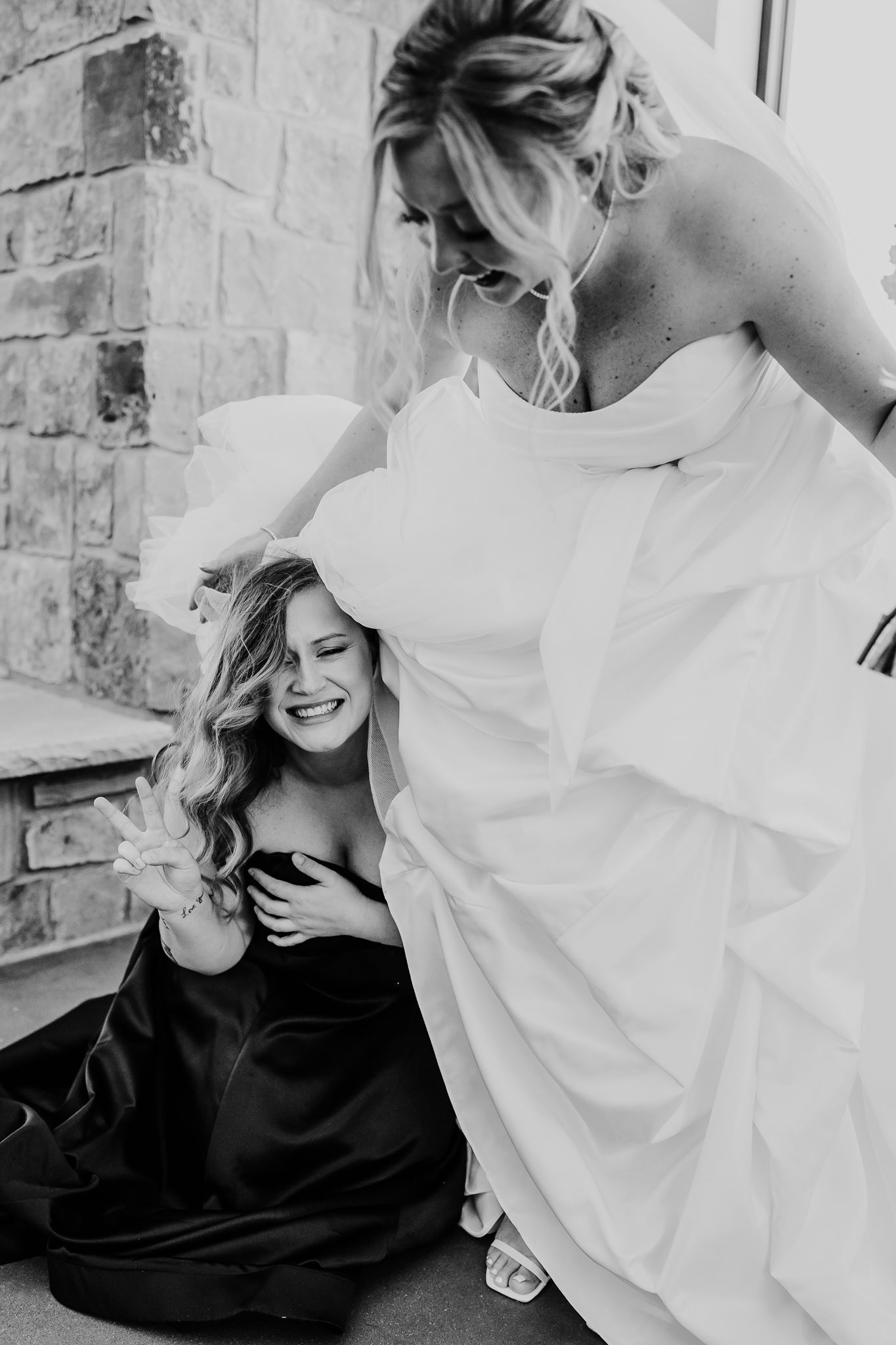 A bridesmaid and bride laugh together on their wedding day.