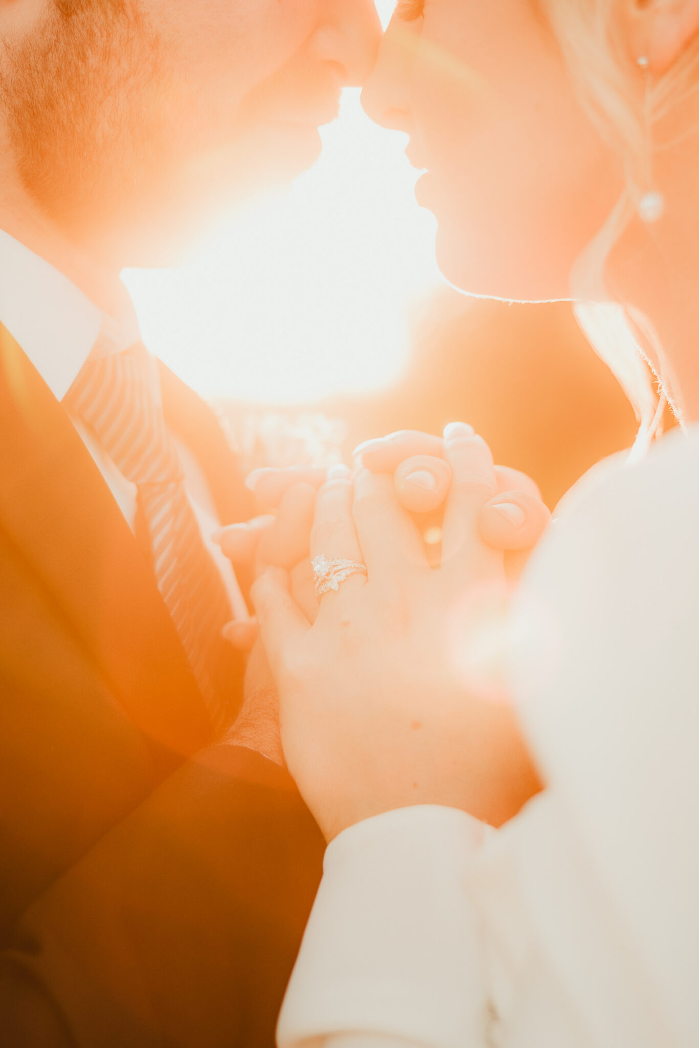 A couple holds hands on their wedding day as the setting sun glows around them,