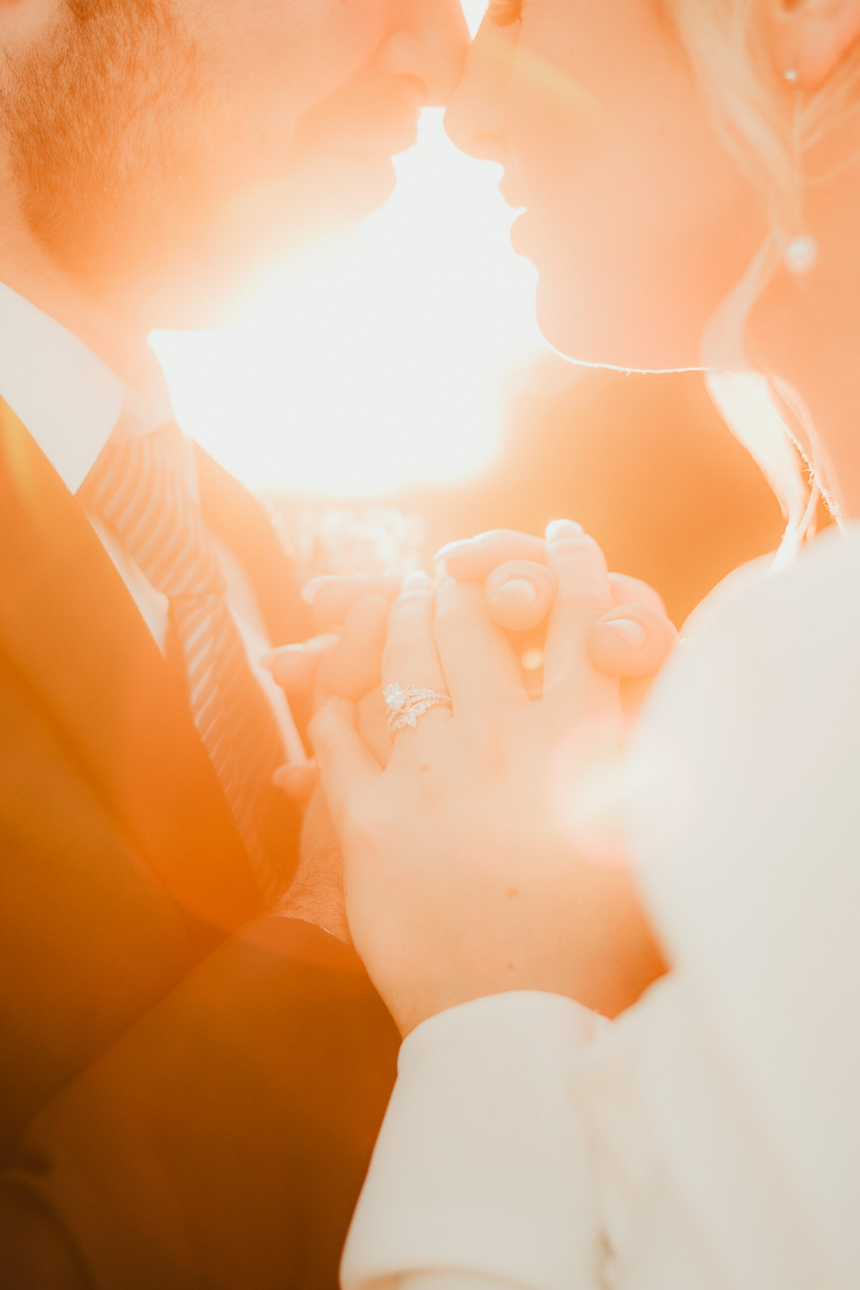 A couple holds hands on their wedding day as the setting sun glows around them,