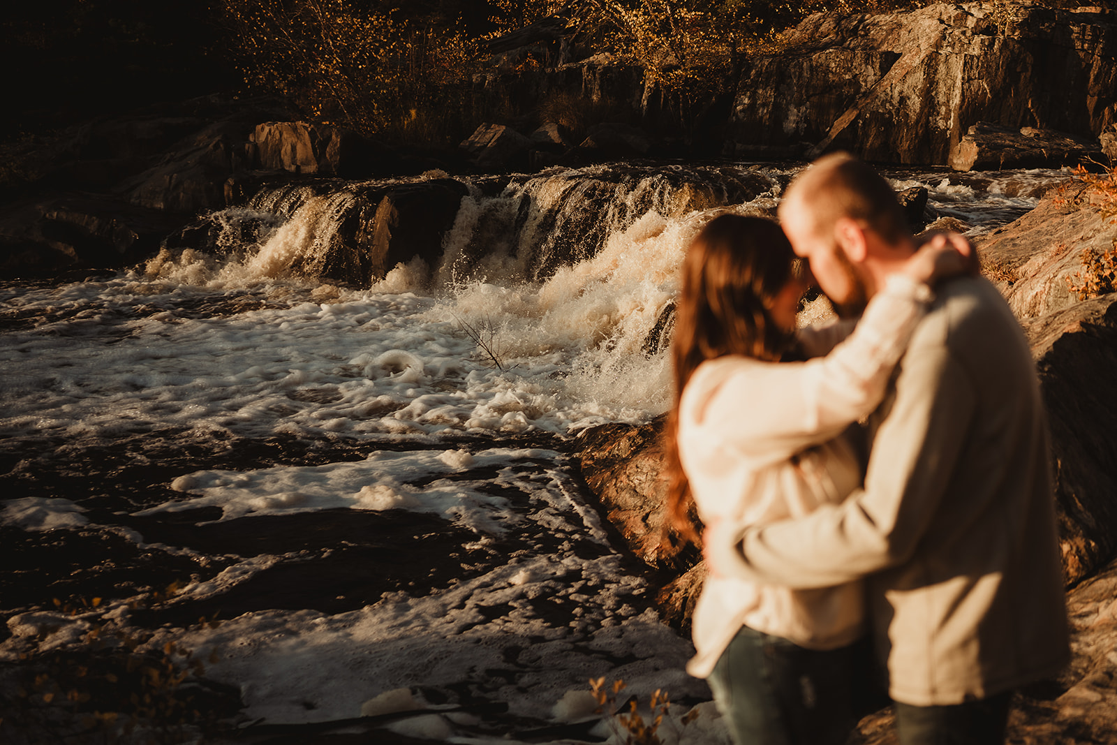 The falls at Big Falls County Park are flowing fast as a couple embrace during their engagement session in Eau Claire.